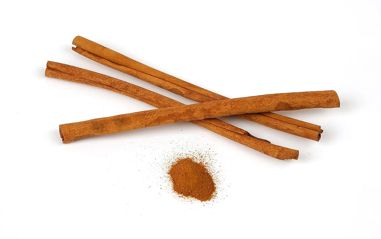 cinnamon sticks with small pile of ground cinnamon on white