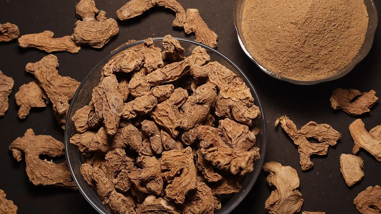dried ginger pieces with small bowl of powdered ginger