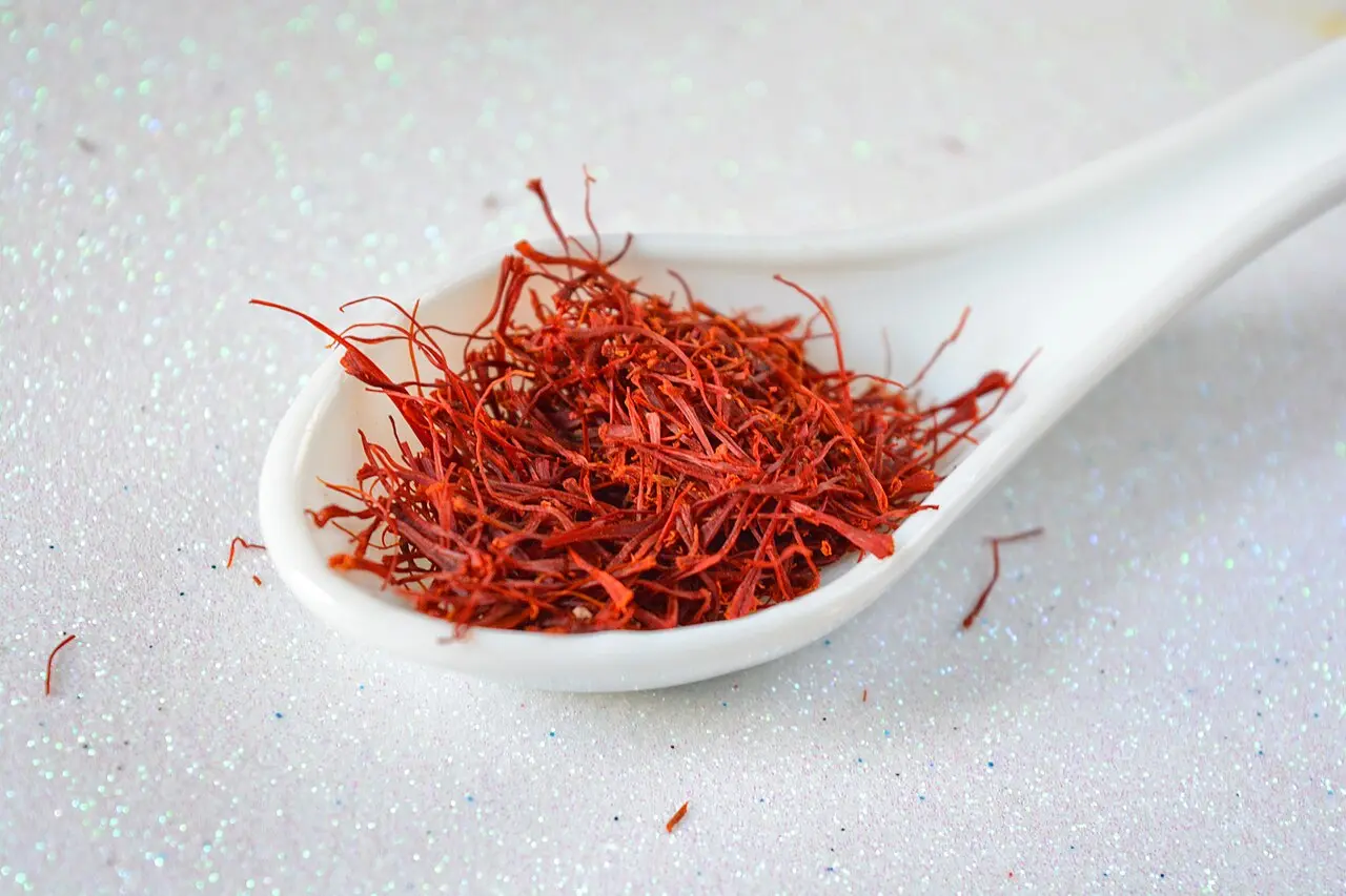 white spoon holding saffron threads on glittery surface